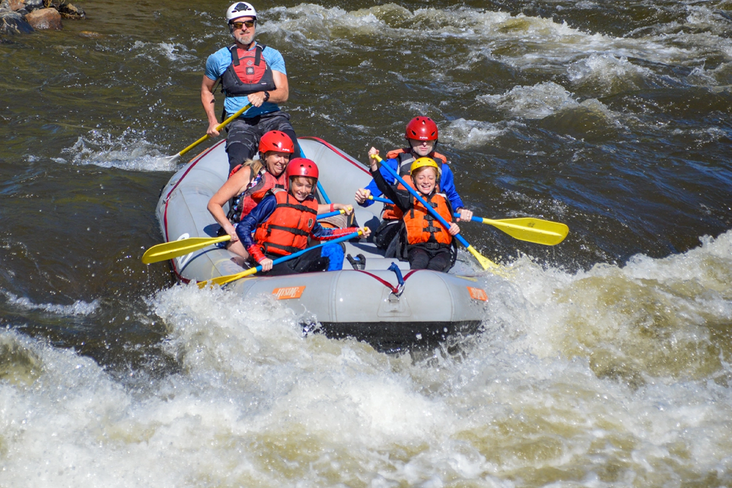 Family smiling while paddling through whitewater in Clear Creek - Idaho Springs, Colorado