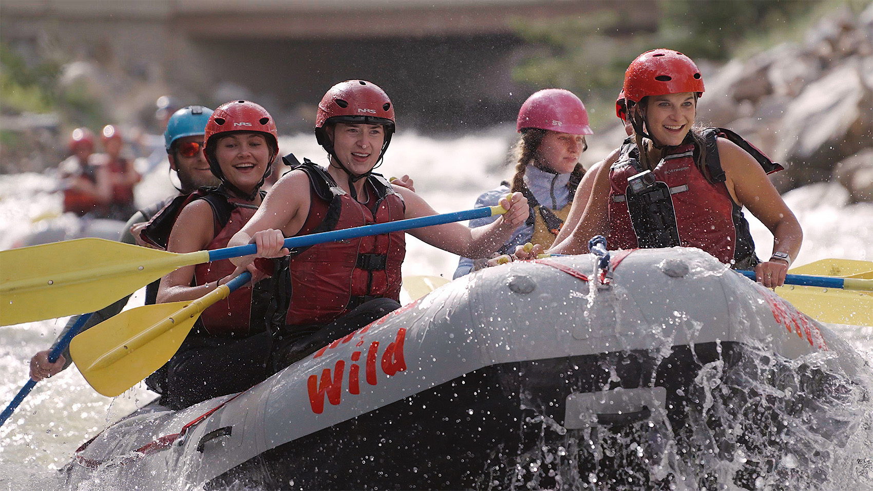 close up of smiling group of rafters in red helmets paddling through white water rapids on Clear Creek near Idaho Springs, Colorado, with a Mild to Wild guide.