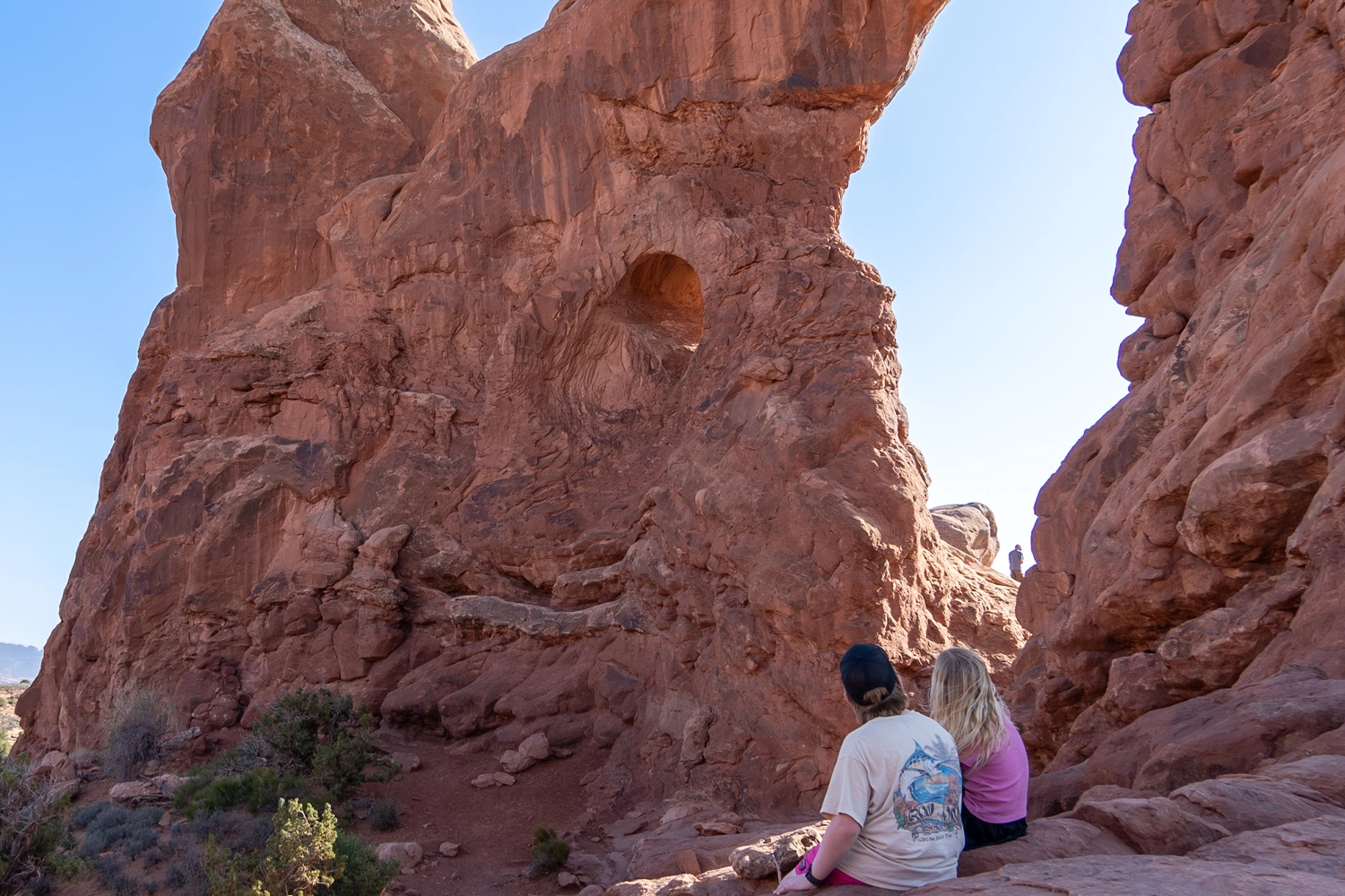 two young kids sitting on rock looking at a large arch in Arches National park