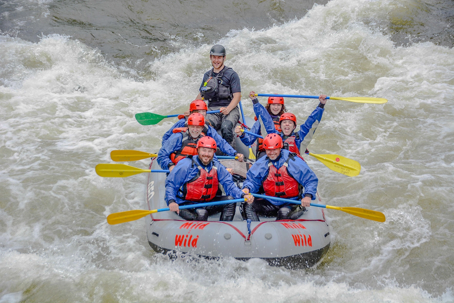Smiling group of rafters in red helmets paddling through white water rapids on Clear Creek near Idaho Springs, Colorado, with a Mild to Wild guide.