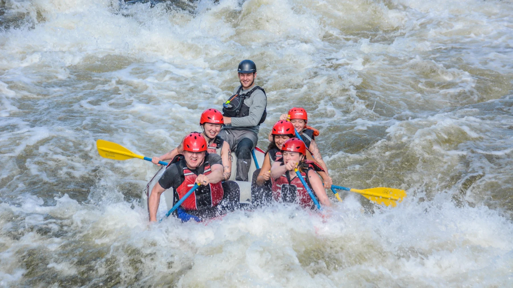 Group of smiling rafters paddling through white water rapids on Clear Creek in Idaho Springs, Colorado, during a Mild to Wild Rafting trip near Denver.