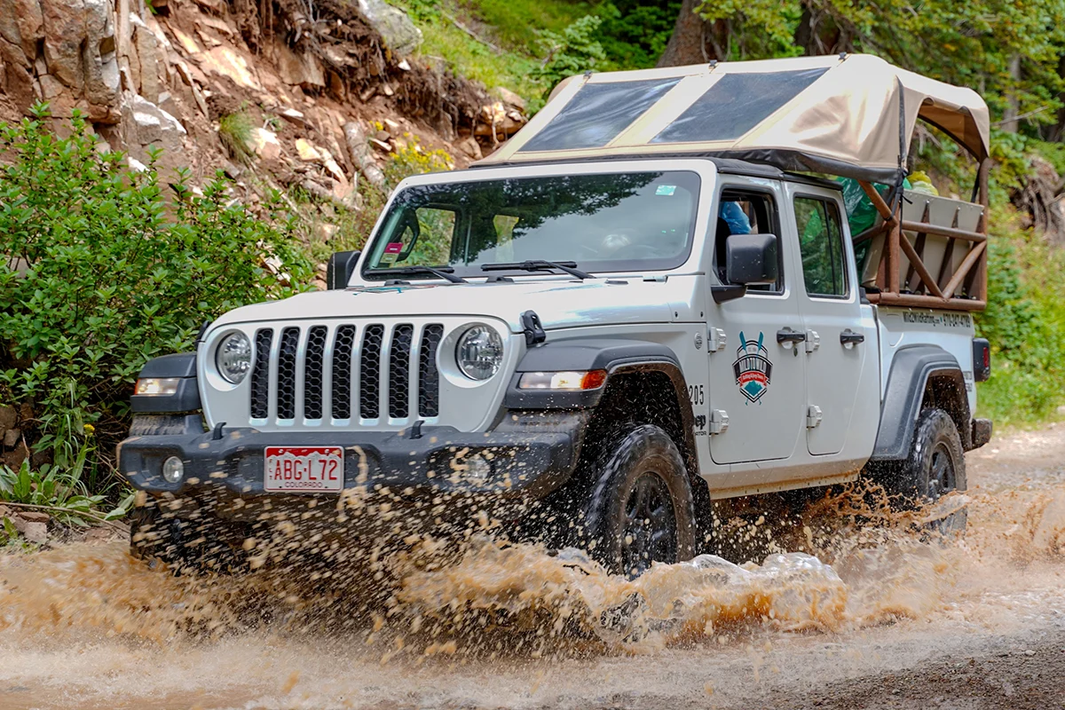 A mild 2 wild tour jeep splashes through a wet mountain road