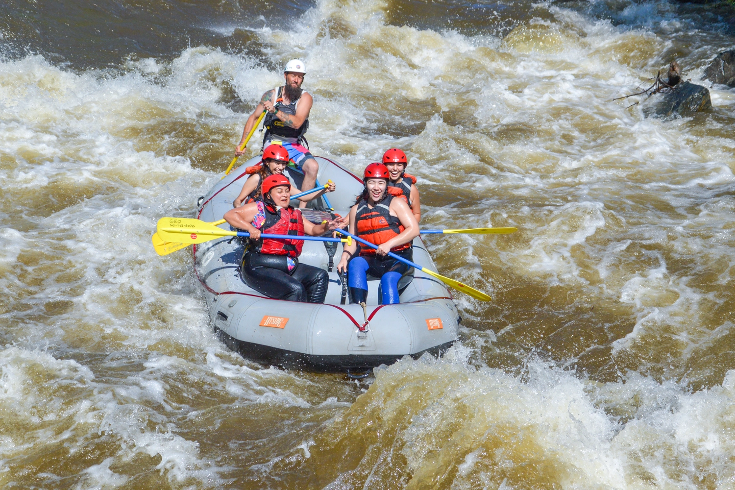 Raft full of smiling guests paddling through whitewater in Clear Creek - Idaho Springs
