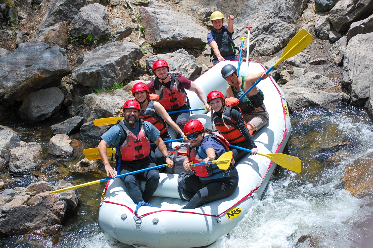 Raft full of smiling guests parked next to rocks in Clear Creek - Idaho Springs, Colorado
