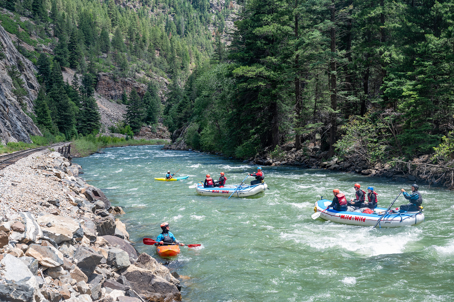 Wide shot down stream of the upper Animas river with rafts and a kayak in frame - train tracks to the left
