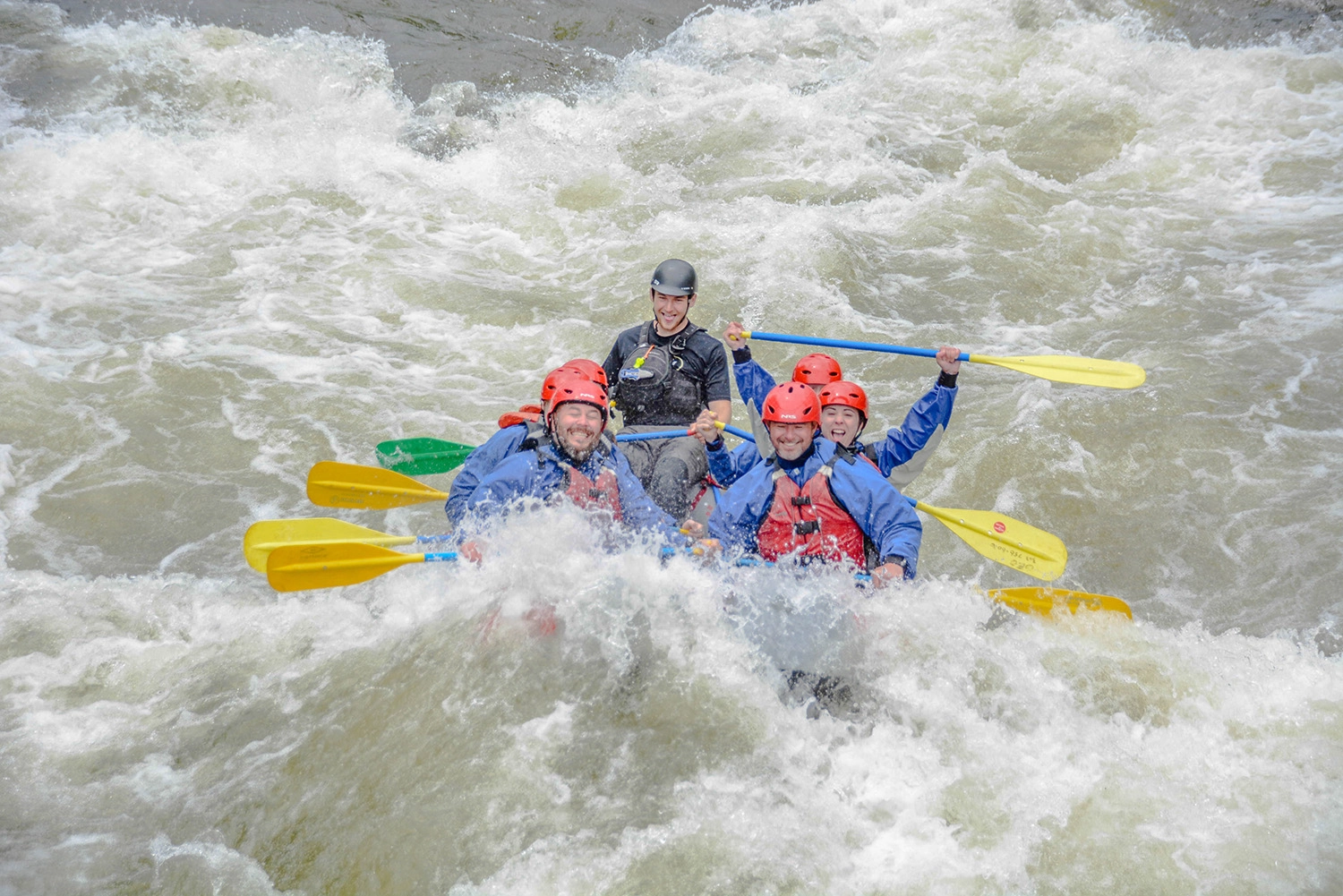 Smiling group of rafters in red helmets paddling through white water rapids on Clear Creek near Idaho Springs, Colorado, with a Mild to Wild guide.