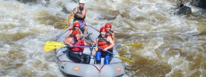 Raft full of smiling guests paddling through whitewater in Clear Creek - Idaho Springs
