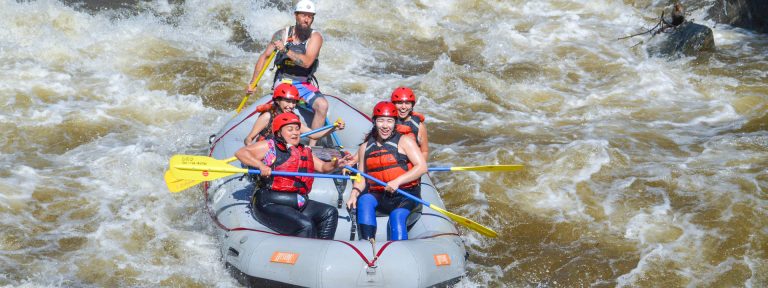 Raft full of smiling guests paddling through whitewater in Clear Creek - Idaho Springs
