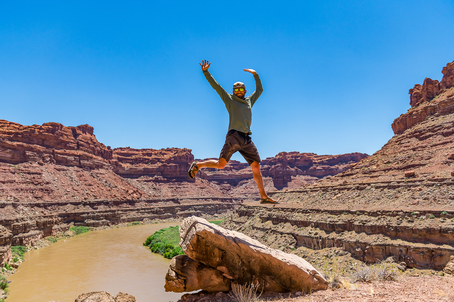 Man jumping into the air with the Colorado River in the backdrop on the loop hike in Cataract Canyon