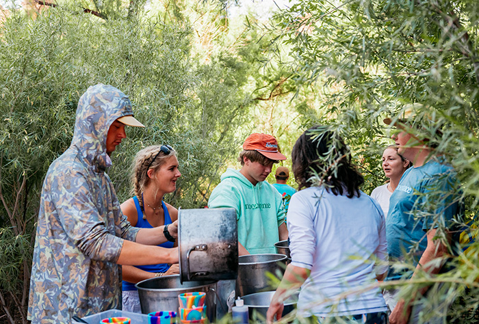 Group getting food around a table in the tamarisk brush of Cataract Canyon