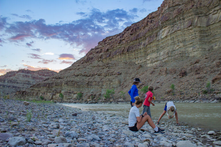 Kids sitting on a rocky beach under the sunset in Desolation Canyon