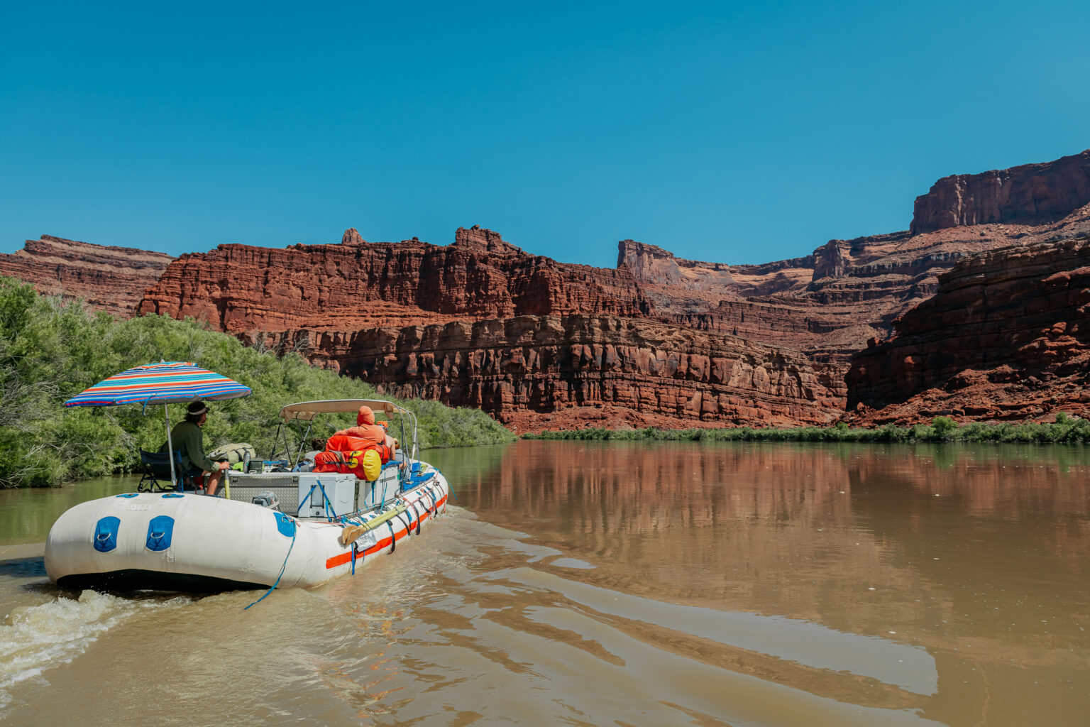 raft motoring through flat water in cataract canyon - blue sky, red rock scenery