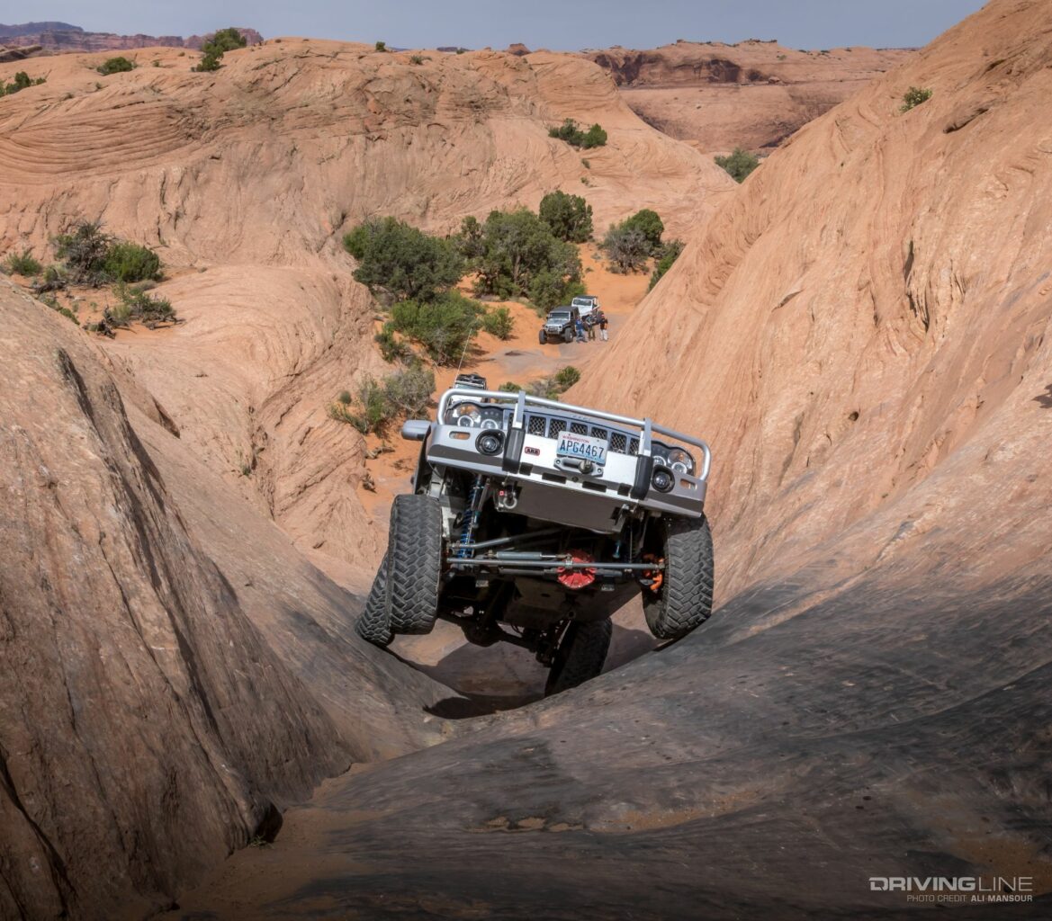 Jeep with one tire in the air going up the sandstone of Hell's Revenge trail in Moab