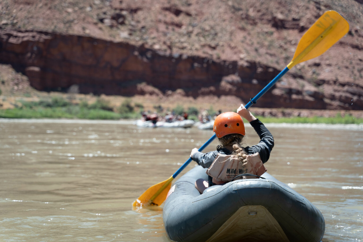 Close-up of kayaker from behind with boats and rock wall in the back