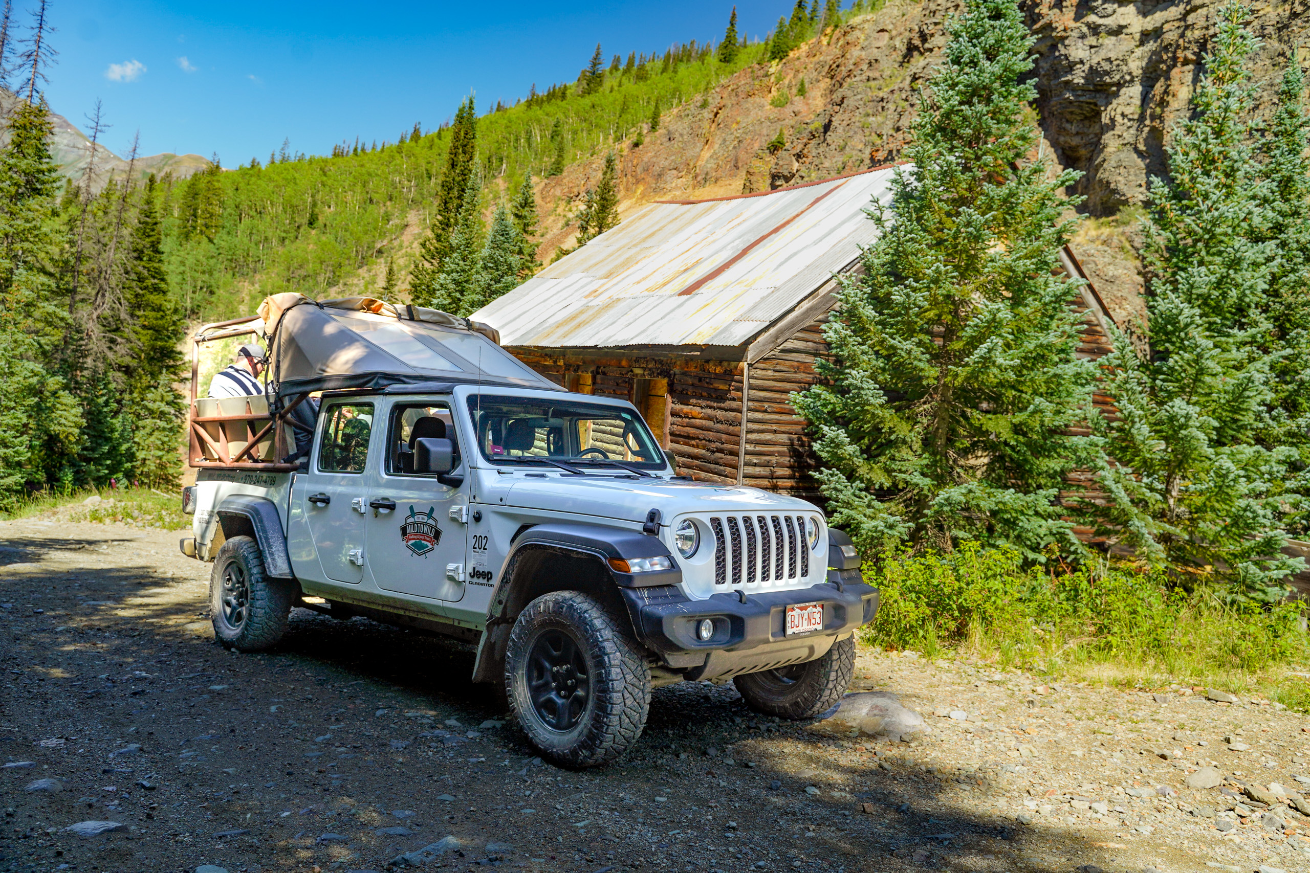 Jeep Gladiator parked in front of abandoned cabin with trees and rock in background - Silverton, CO - Mild to Wild