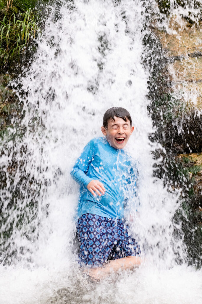 young boy standing under small waterfall getting soaked - butt dam falls - Gates of Lodore