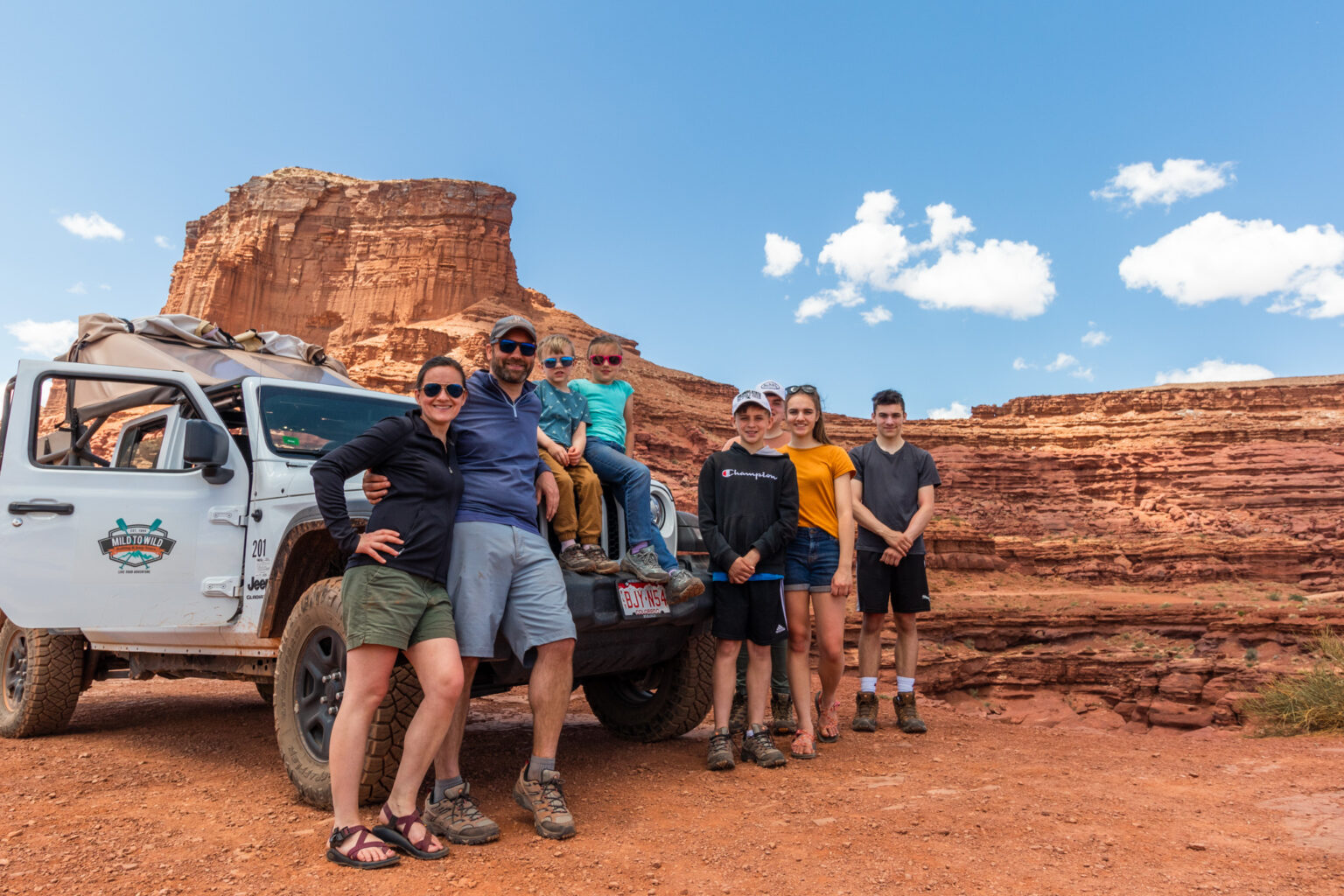 Family posing for a photo in front of a mild to wild jeep gladiator - Moab Utah