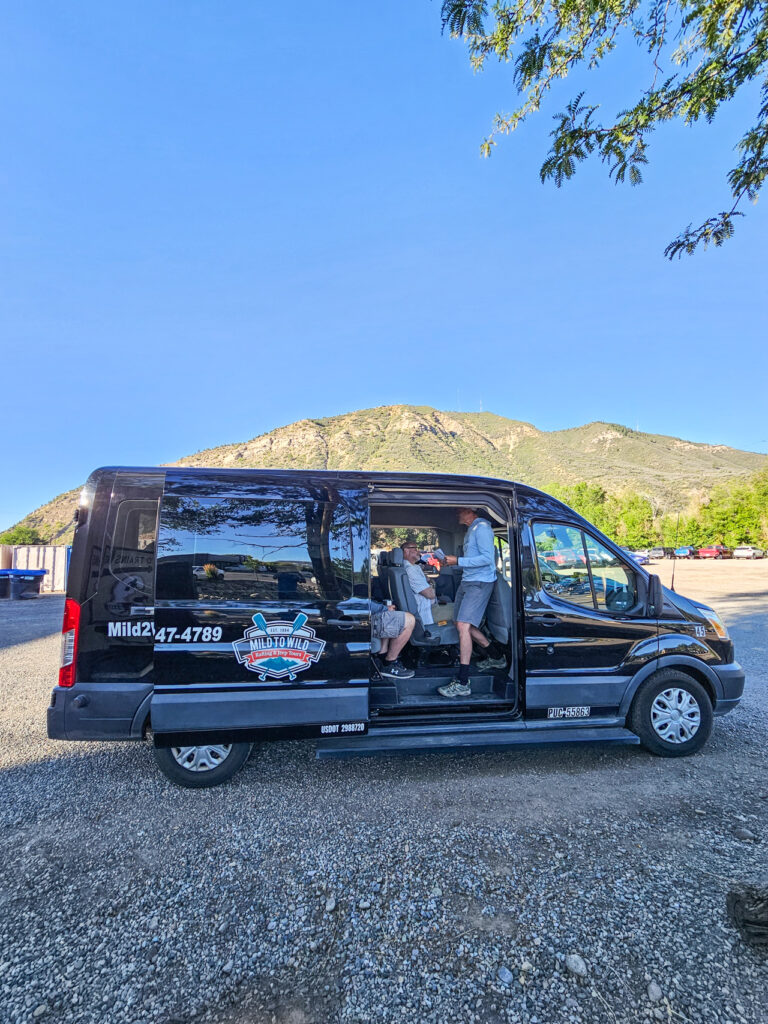 Medium shot of Mild to Wild black Passenger Van with Mountains behind