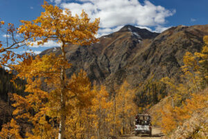 Wide shot of Silverton fall colors with jeep driving on dirt road