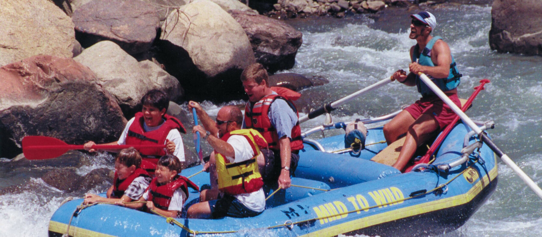 close up of blue mild to wild raft going through smelter whitewater park - kids in front getting splashed - smiles