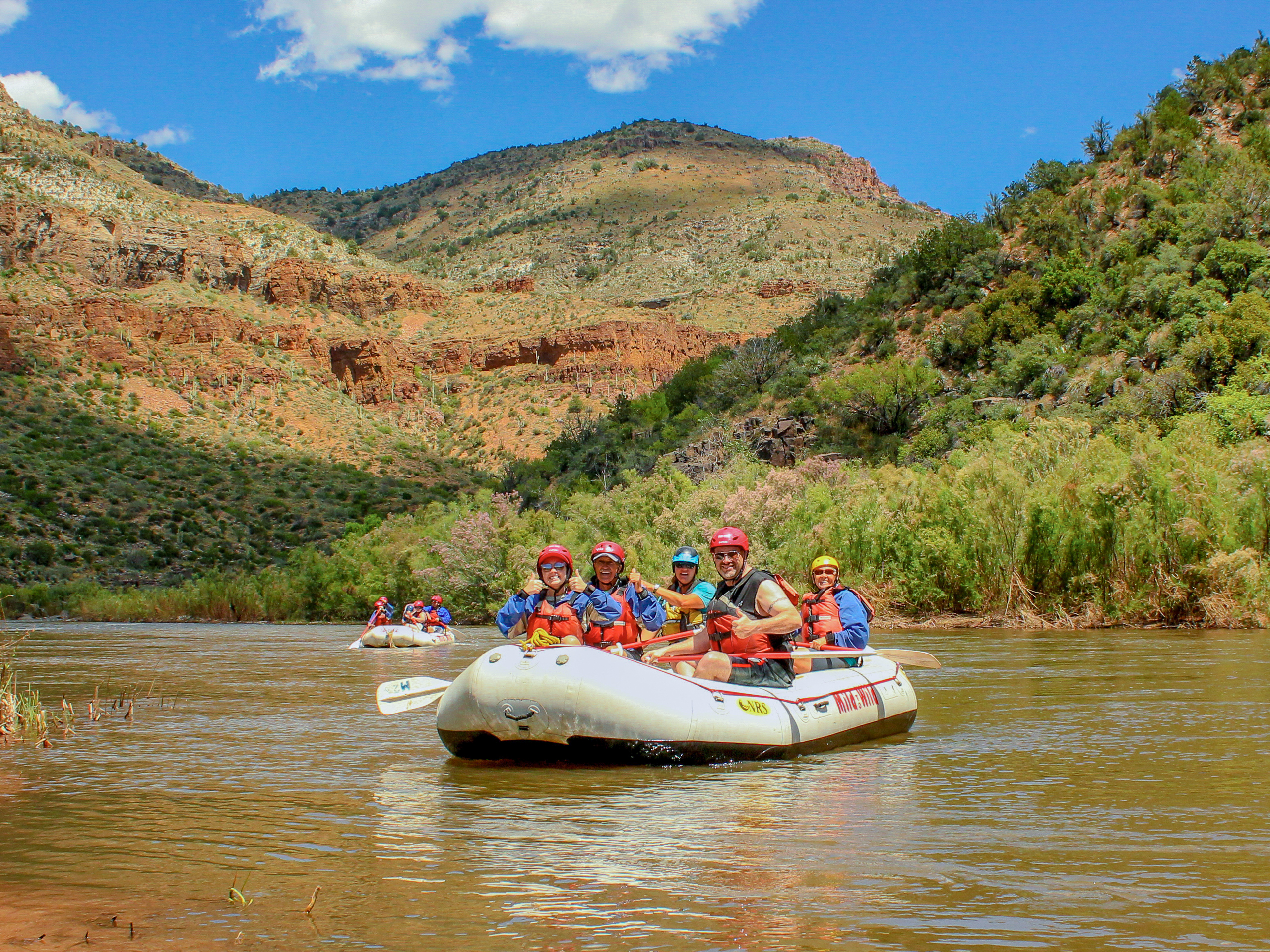 Raft full of people smiling on a calm section of the Upper Salt River with cliffs in the background