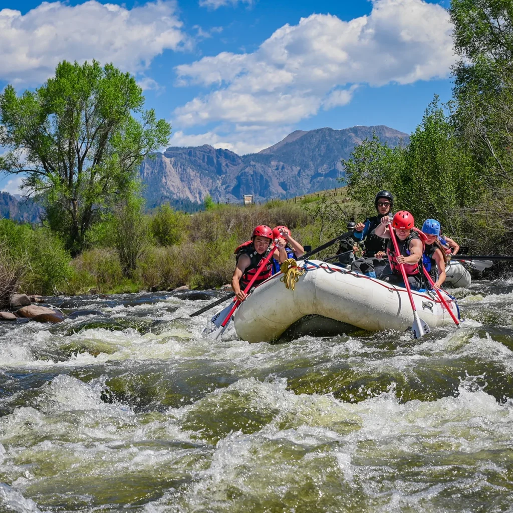 A medium shot of a river rafting group paddling through rapids on the Piedra river with mountains in the background