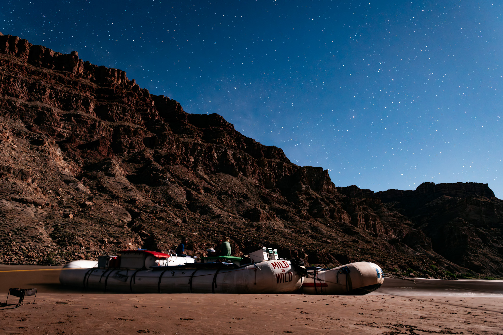 Boats along the riverbank with a starry sky in the background.