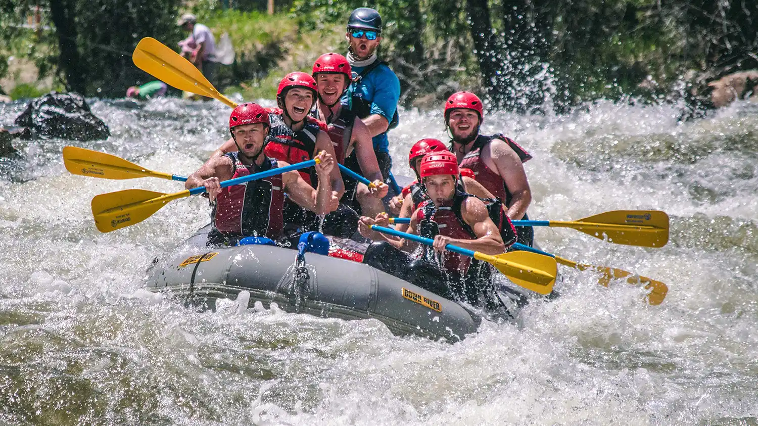 Arkansas River rafting group of seven wearing helmets, life jackets, and holding paddles as they ride the waves