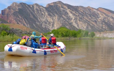 medium shot of a raft on the yampa river with guests on the boat and beautiful faults in the background